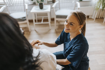 High angle view of smiling healthcare worker crouching near female patient at care home