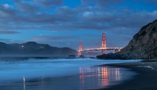 View of illuminated golden gate bridge over sea against cloudy sky at night