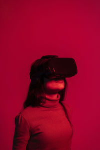 Mid adult woman using virtual reality headset while standing against red background