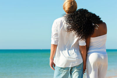 Rear view of women standing at beach against clear sky