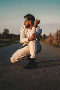 Side view of young man standing on road against sky