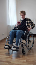 Full length of young man using phone sitting on wheelchair