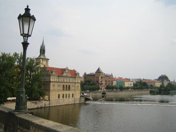 Street light by river against buildings in city against sky