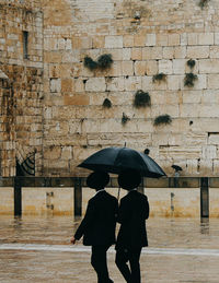 Full length of wet woman walking on cobblestone during rainy season