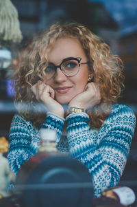 Thoughtful young woman looking away while sitting in cafe seen through glass window