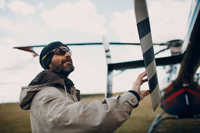 Side view of man holding camera against sky