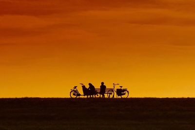 Silhouette man riding bicycle on grass against sky during sunset