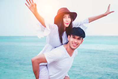 Portrait of smiling husband piggy backing wife while standing at beach