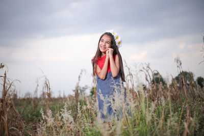 Smiling cute girl standing amidst plants on field during sunset