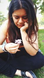 Thoughtful young woman with flower sitting on grassy field