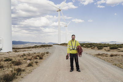 Engineer with helmet and rope standing on road at wind farm