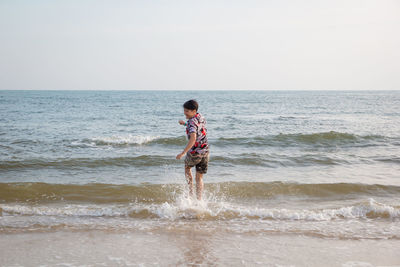 Happy man running at beach against sky