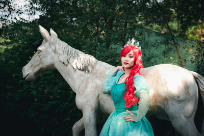 Portrait of smiling woman wearing crown with red hair standing by sculpture