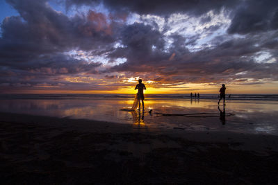 Men standing on beach against cloudy sky during sunset