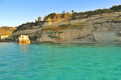 Rock formations in sea against clear blue sky