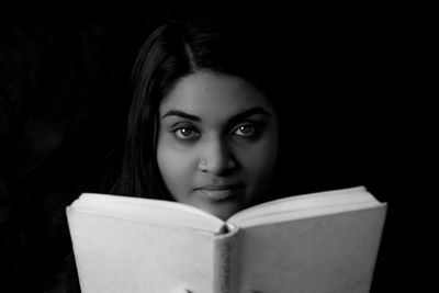 Close-up portrait of woman holding book against black background