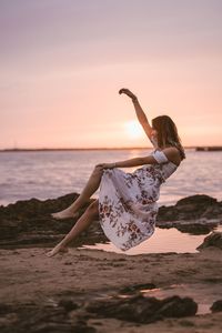 Woman levitating at beach against sky during sunset