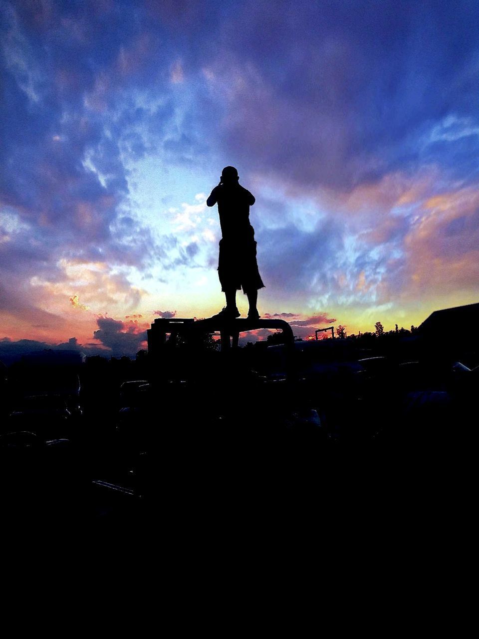 SILHOUETTE OF MAN WITH ARMS RAISED AGAINST SKY DURING SUNSET