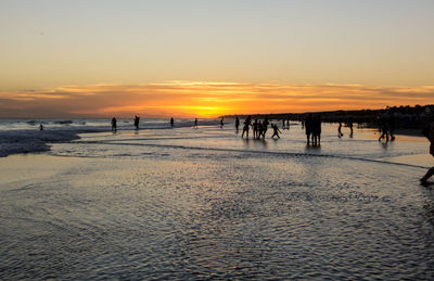 Silhouette people on beach against sky during sunset