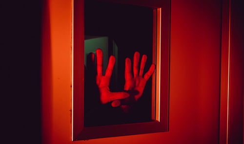 Close-up of hands pressed against window with red illumination