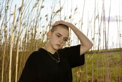 Young woman looking away while standing on field against sky