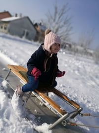 Girl sitting on sledge at snow covered field