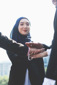 Smiling young businesswoman stacking hands with colleagues