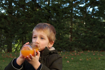 A blond boy drinks orange juice from a glass bottle.