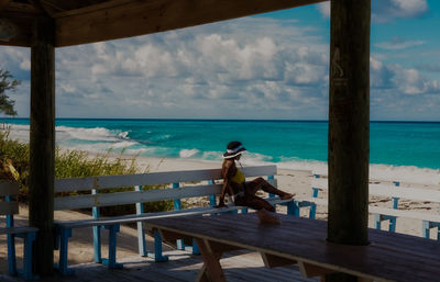 Side view of woman relaxing on seat by sea against sky