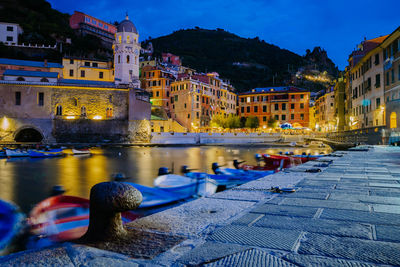 Boats in canal by illuminated buildings in city at night