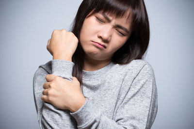 Young woman with arm pain against gray background