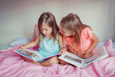 Sisters reading books while sitting on bed at home