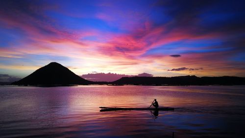 Silhouette man on lake against sky during sunrise 