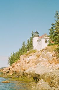 Lighthouse by sea against clear blue sky