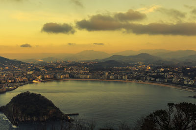 Bridge over river and buildings against sky during sunset