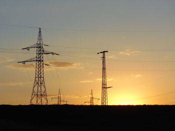 Low angle view of silhouette electricity pylons against the sky