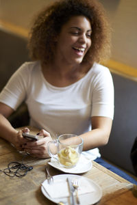 Smiling young woman holding mobile phone while sitting in restaurant