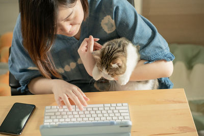 Asian woman play with her cat and use tablet meeting and working from home