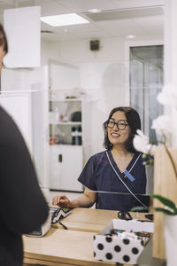 Smiling female receptionist wearing eyeglasses assisting patient at checkout in hospital