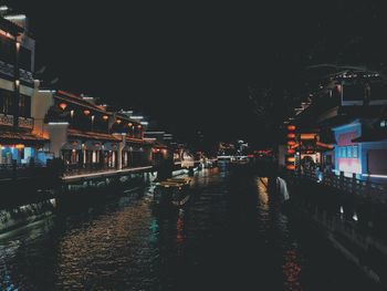 Illuminated buildings by street against sky at night