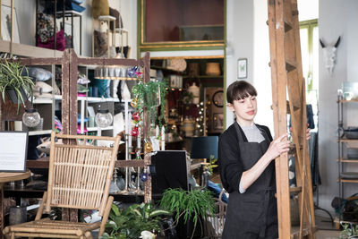 Young female entrepreneur carrying ladder at store