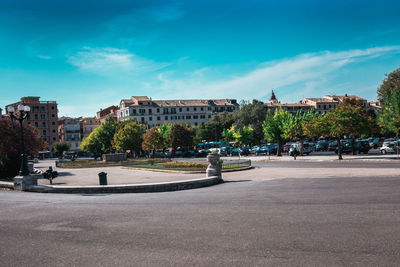 Road by trees and buildings against blue sky