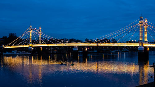 Illuminated bridge over calm river against blue sky