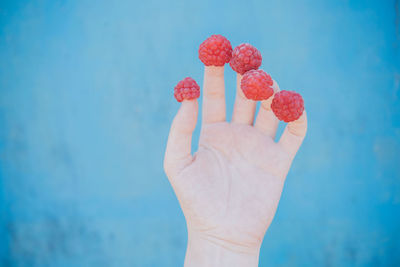 Close-up of hand holding strawberry against blue sky