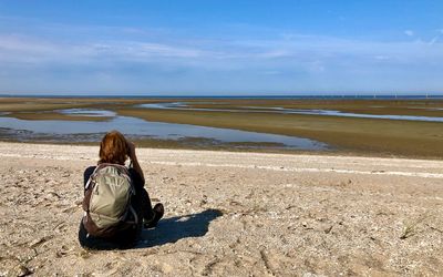 Rear view of woman standing at beach against sky