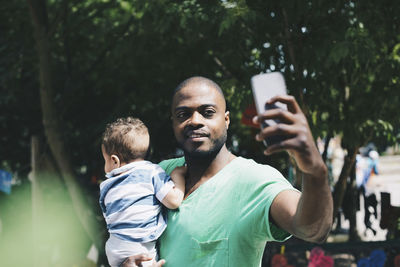 Father taking selfie through smart phone while carrying son at park