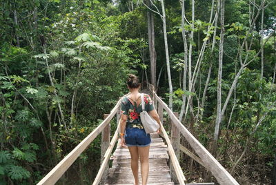 Rear view of woman walking on footbridge in forest