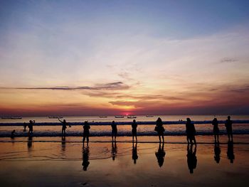 Silhouette people on beach against sky during sunset