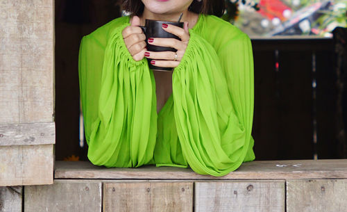 Woman in green shirt holding a cup of coffee leaning out on a window