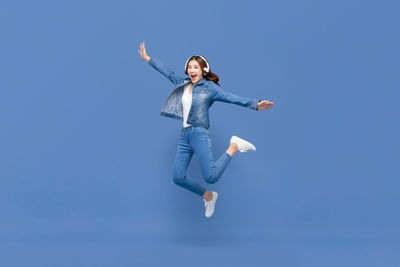 Full length of young woman jumping against clear blue sky